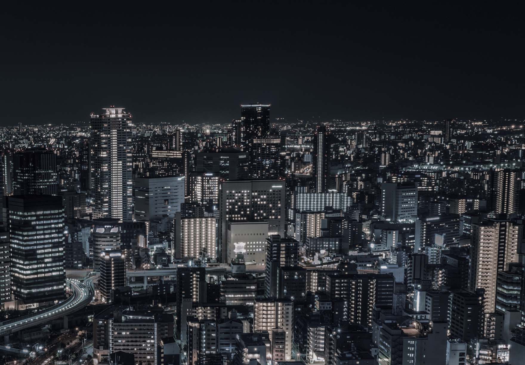 夜空に浮かび上がる高層ビル群が明かりに照らされ、暗い空の下に密集した都市のスカイラインを描き出す、活気に満ちた街の夜景。このシーンは、街の活気と賑わいを際立たせています。.