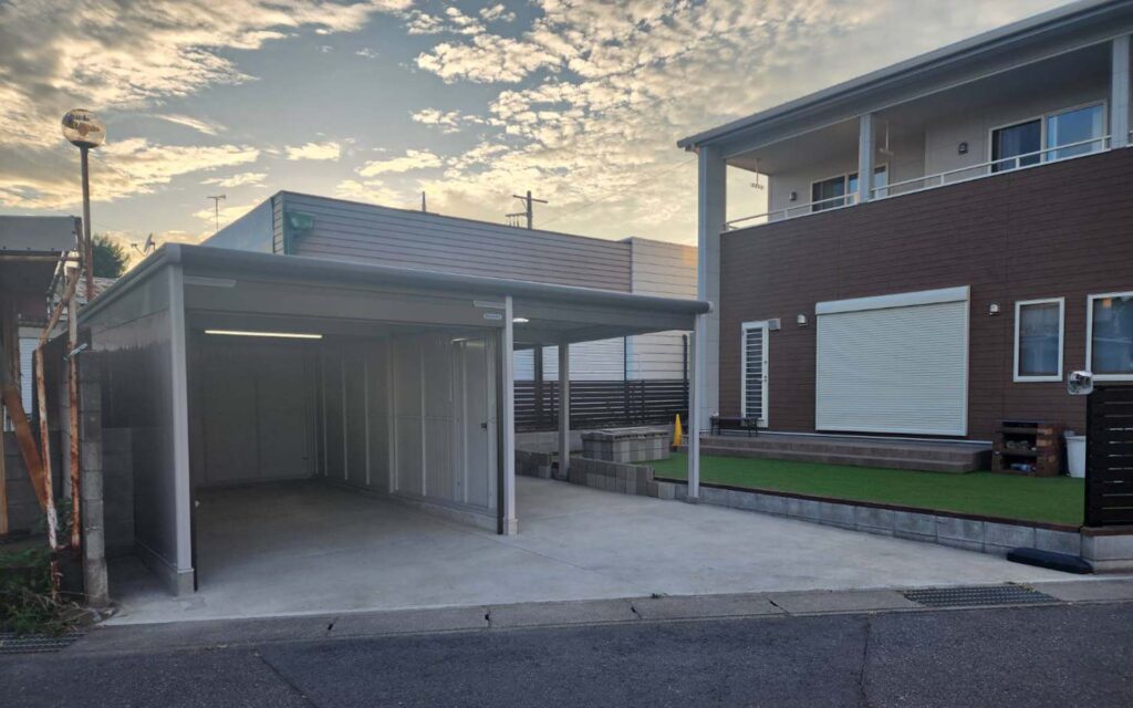 茶色と白の外観、屋根付きのカーポート、人工芝の芝生、背景に散らばった雲のある晴れた空を備えたモダンな家。.